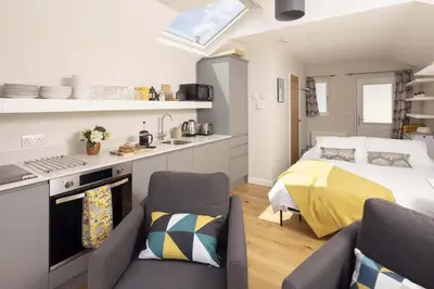 a bedroom with a bed and a kitchen with a couch at Stylish Boatshed with Sea Views Private Parking in Gorran Haven