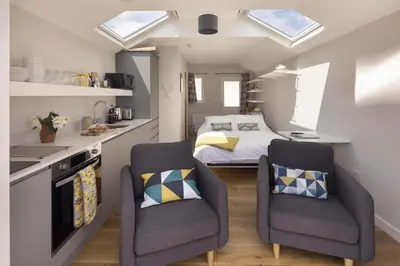a small kitchen with two chairs and a bed at Stylish Boatshed with Sea Views Private Parking in Gorran Haven