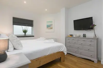 a white bedroom with a bed and a tv at Captain's Walk in Newquay