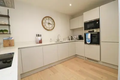 a kitchen with white cabinets and a clock on the wall at Fifty Steps from the beach! in St Merryn