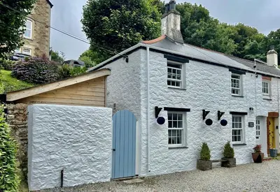 a white building with a garage and a house at Engellie Cottage in Perranporth
