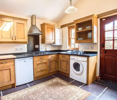 a kitchen with wooden cabinets and a washer and dryer at Mona's Cottage - Private Parking, Sea Views, Garden & Close To Harbour & Beach in Charlestown