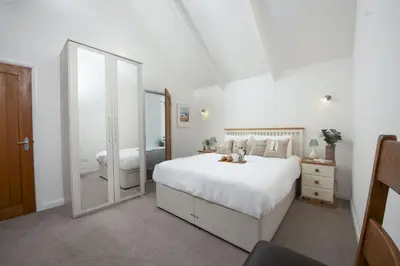a bedroom with a large white bed and a mirror at Samson Cottage in Saint Mawgan