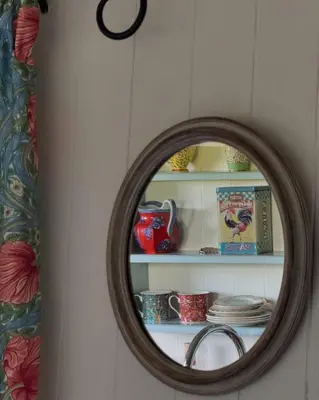 a mirror on a wall with a shelf with dishes at Elderflower Hut in Port Isaac