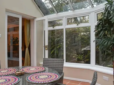 a conservatory with a table and chairs on a patio at Byre Cottage in Fowey