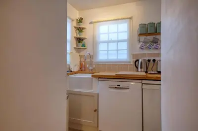 a white kitchen with a sink and a window at Grade II Listed Cottage Gorran Haven Sea Views in Gorran Haven