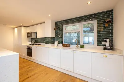 a kitchen with white cabinets and a brick wall at Luxury Cornish Seaview Bungalow in Looe
