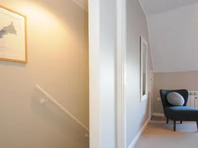 a hallway with a blue chair and a stair case at Sea Spray in Port Isaac