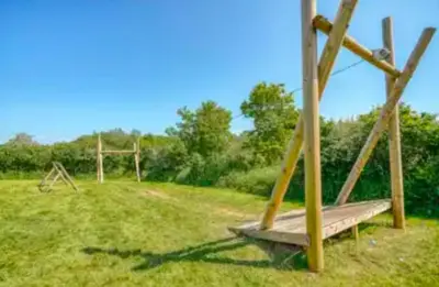 a wooden swing set in a grassy field at Wallows Lodge with private hot tub in St Austell