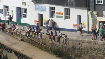 a group of people sitting on a wall near a train at Wild Air Guest House in Mevagissey