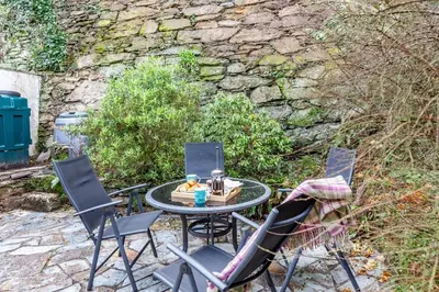 a patio table with three chairs and a stone wall at 2 Bed in Polruan oc-g30534 in Fowey