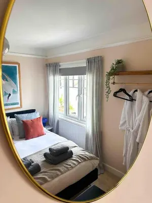 a mirror reflecting a bedroom with a bed and a window at Skylark House Padstow, Stylish Victorian Townhouse, Private Sauna, Cold Plunge and Log Burner in Padstow