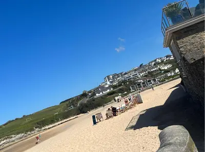 a beach with a group of people sitting on the sand at Peaceful room near to beach - Newquay Porth in Saint Columb Minor