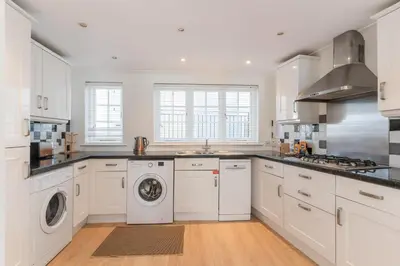 a kitchen with white cabinets and a washer and dryer at The White House in Wadebridge