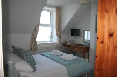 a bedroom with a bed with a desk and a window at Rivendell Guest House in St Ives