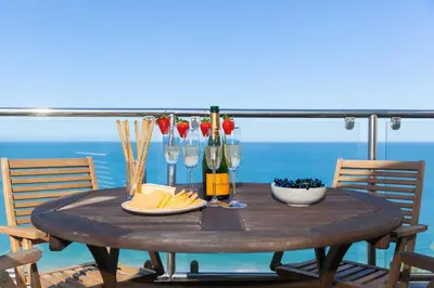 a wooden table with glasses and wine bottles on a balcony at Coastal Breeze in Carbis Bay