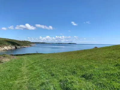 a grassy hill with a view of a body of water at Coastal house, large garden, 4 bedrooms, 2 bathrooms, BBQ, 10 min walk to beach in Mawnan Smith