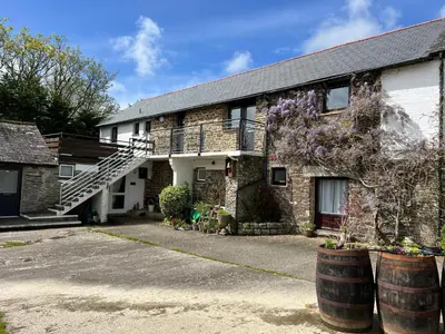 an old stone house with two barrels in front of it at Hop Loft-Barn Conversion, with access to Pool & Hot Tub-at Fox Valley Cottages in Looe