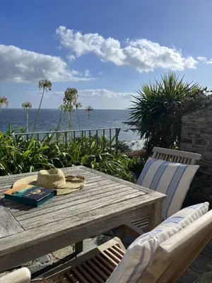 a wooden table and chairs with the ocean in the background at Pengerein in Porthscatho