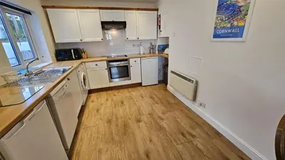 a kitchen with white cabinets and a wooden floor at Pengerein in Porthscatho