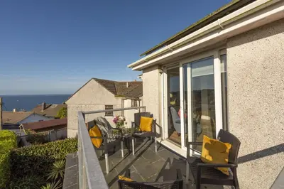 a balcony with yellow pillows and chairs on a house at Ocean Parc in Carbis Bay