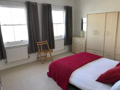 a bedroom with a bed and a chair and windows at 5 Hatfield Cresent in Newquay