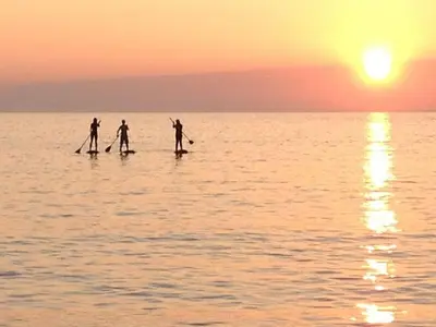 three people are paddle boarding on the water at sunset at Rock Cottage in St. Issey