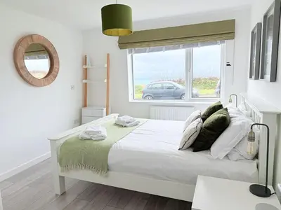 a white bedroom with a bed and a window at 8 Coastline Apartment in Newquay