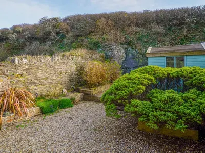 a garden with a stone wall and some bushes at Skiber An Hyli in Mawgan Porth