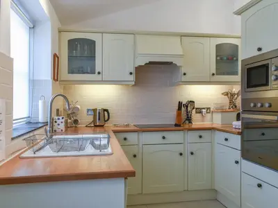 a kitchen with white cabinets and a sink at Skiber An Hyli in Mawgan Porth