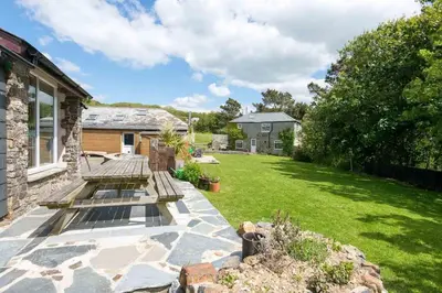 a backyard with two benches on a stone patio at Abel's Cottage gorgeous character barn Crackington in Crackington Haven