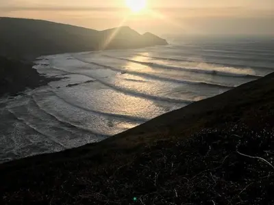 a sunset over a beach with the sun shining on the water at Abel's Cottage gorgeous character barn Crackington in Crackington Haven