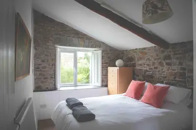 a bedroom with a bed with red pillows and a brick wall at Abel's Cottage gorgeous character barn Crackington in Crackington Haven