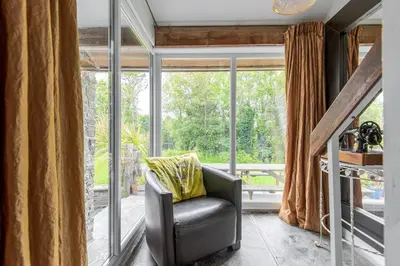 a living room with a chair in front of a window at Abel's Cottage gorgeous character barn Crackington in Crackington Haven