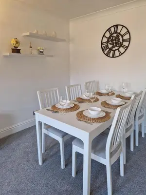 a white dining room table with white chairs and a clock at Harbour View apartment in Portreath in Portreath