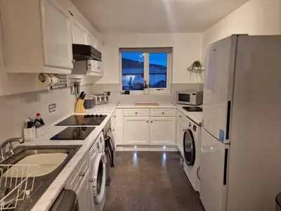 a white kitchen with a refrigerator and a window at Harbour View apartment in Portreath in Portreath