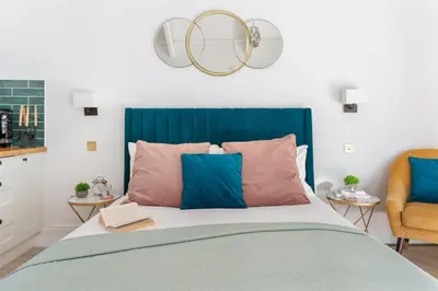 a bedroom with a bed with a blue headboard and two chairs at The Little Pines - 5 min walk to beach and sauna in Falmouth