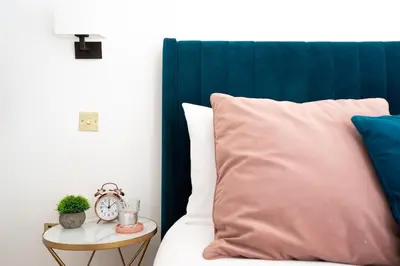 a bed with a blue headboard and a table with a clock at The Little Pines - 5 min walk to beach and sauna in Falmouth