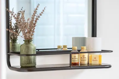 a shelf with bottles of essential oils and a mirror at Stylish cottage, log burner - Tregavone Cottage in Falmouth