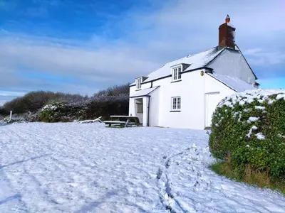 a white house with snow on the ground at Lower Tresmorn Cottage in Crackington Haven