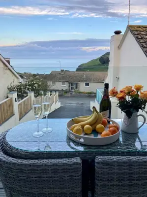 a plate of fruit on a table with a bottle of wine at Kittiwake Retreat, a luxury escape by the sea! in Gorran Haven