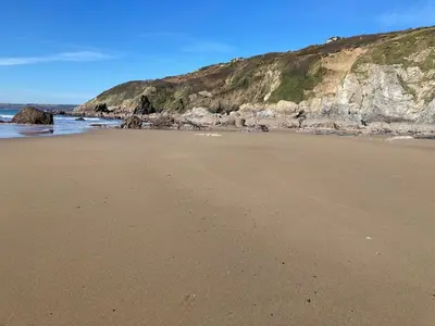 a sandy beach next to a cliff with the ocean at Kittiwake Retreat, a luxury escape by the sea! in Gorran Haven