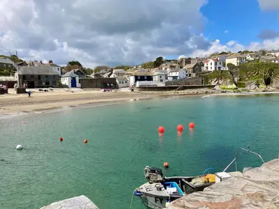 a boat in the water next to a beach at Kittiwake Retreat, a luxury escape by the sea! in Gorran Haven