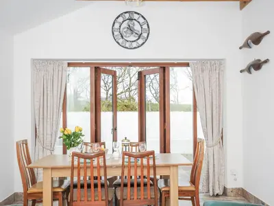 a dining room table with chairs and a clock on the wall at The Dairy Barn in Camelford