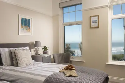 a teddy bear sitting on a bed in a bedroom with windows at Beachside Fistral, Newquay in Newquay