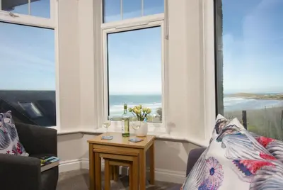 a living room with windows and a table with flowers at Beachside Fistral, Newquay in Newquay