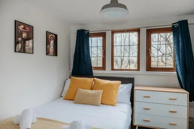 a small bedroom with a bed and two windows at Heron's Perch- A pond-side retreat with cinema room in Callington