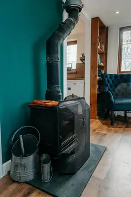 a black stove in a living room with a blue wall at Heron's Perch- A pond-side retreat with cinema room in Callington