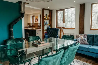 a living room with a glass table and green chairs at Heron's Perch- A pond-side retreat with cinema room in Callington