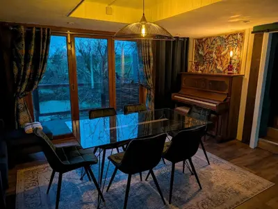 a dining room with a glass table and a piano at Heron's Perch- A pond-side retreat with cinema room in Callington